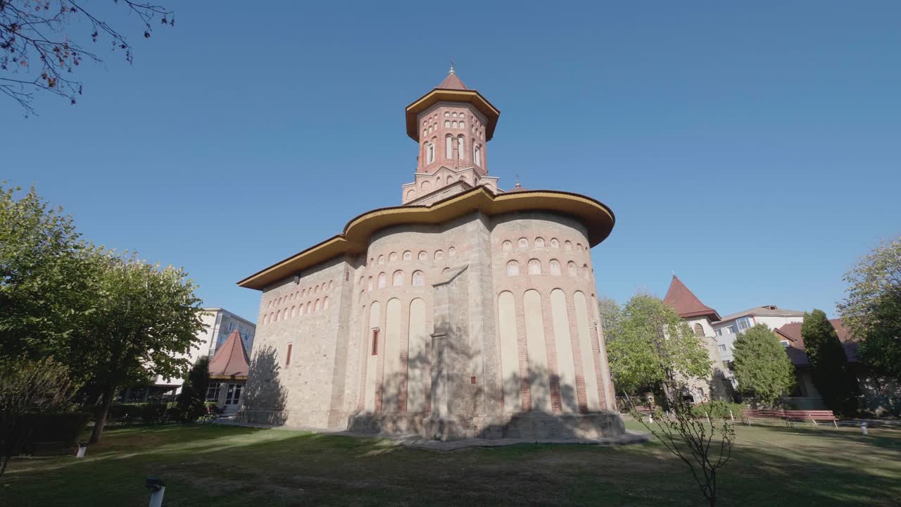 A cinematic dolly shot moves forward towards the historic Precista Church in Bacau, Romania. The medieval Orthodox landmark is set in a green park on a sunny summer day