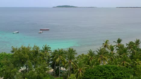 Boats-anchored-in-tropical-ocean-of-Mentigi-Bay-Lombok-with-Gili-Islands-on-horizon,-aerial