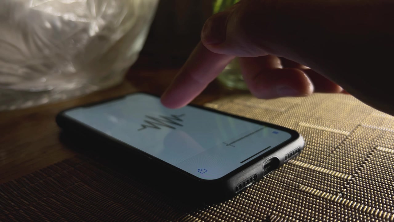 Close-up shot of a hand turning off an audiobook app on a smartphone and placing a wireless earbud on the table. Ideal for digital media and technology visuals.