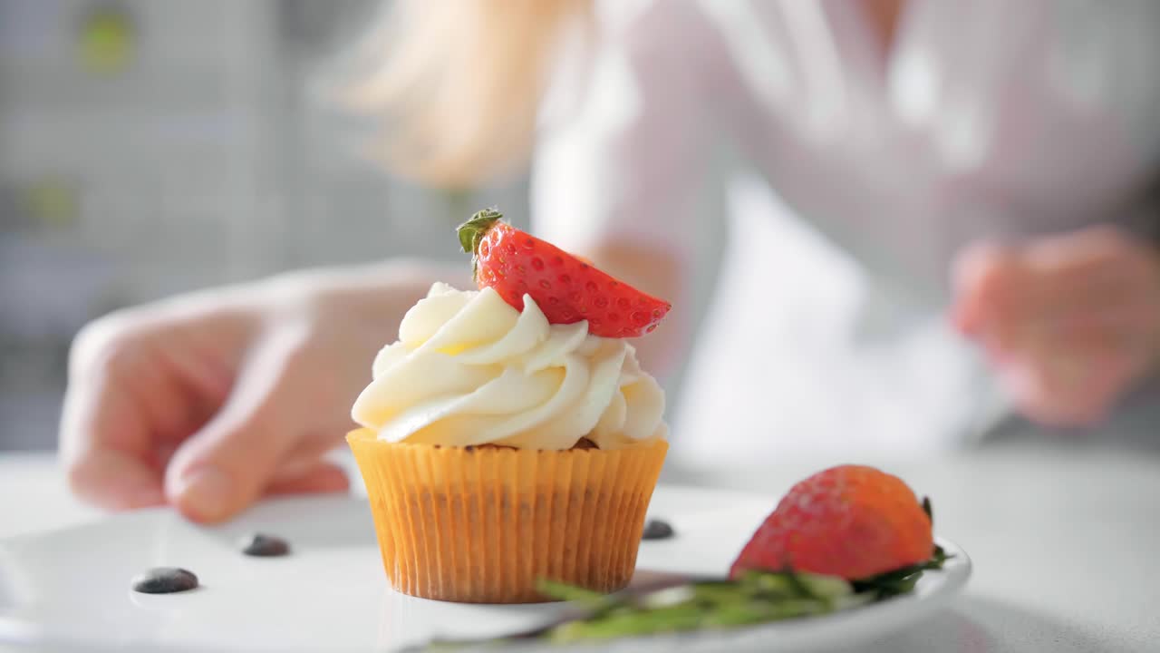 A chef decorating a cupcake with strawberries and cream