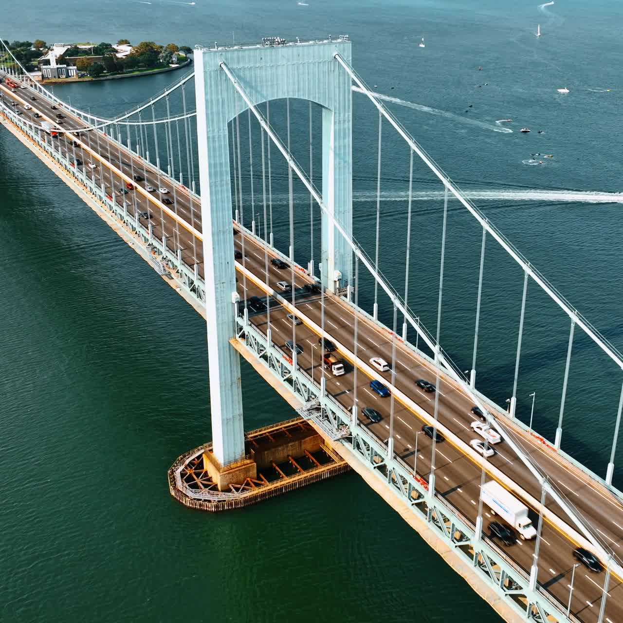 Cars going to and from the Bronx, New York. Aerial view of the Throgs Neck Bridge on sunny day. Boats sailing on the East River at backdrop