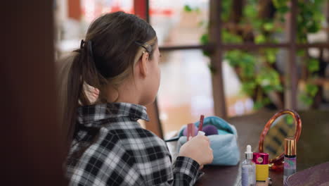 vista trasera de una joven identificando artículos cosméticos en la mesa mientras elige lápiz labial, está rodeada de artículos esenciales de maquillaje, un espejo y accesorios elegantes en un entorno centrado en la belleza