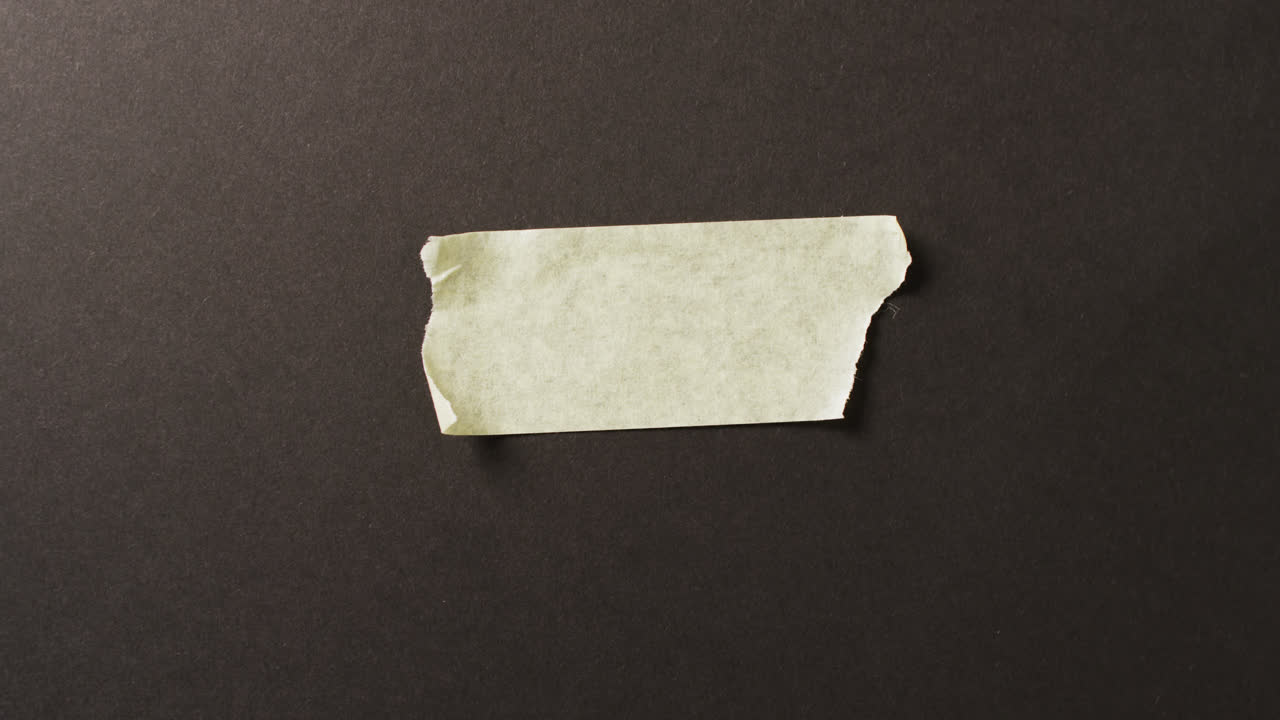 Video of close up of yellow paper tape piece on black background