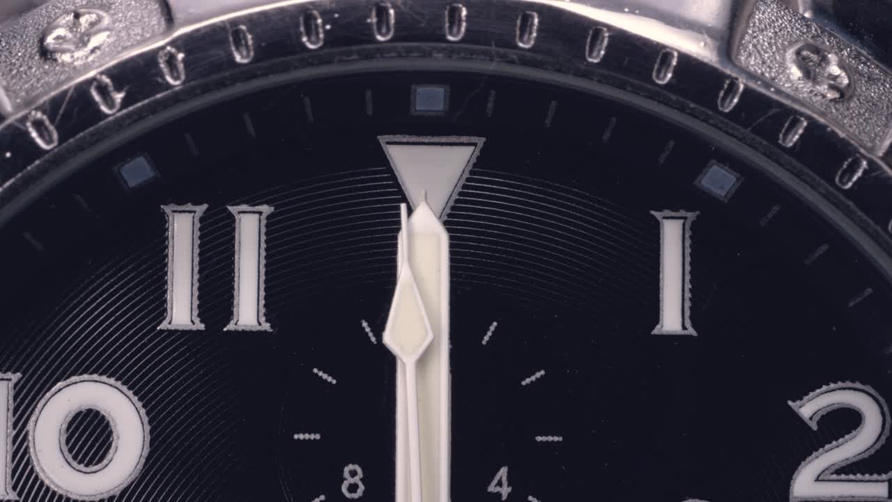 A wristwatch dial with hands passing 12 o'clock. Close up shot.
