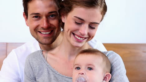 Happy-parents-sitting-on-bed-with-their-baby-son