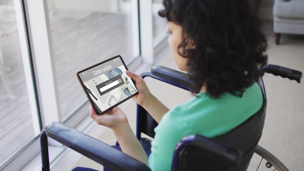 mujer biracial en silla de ruedas usando tableta, compras en línea de ropa, cámara lenta