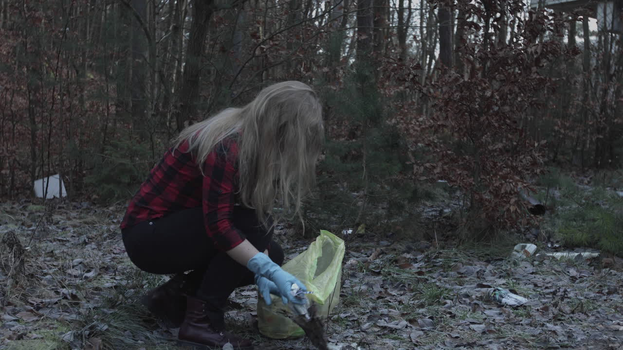 Female ecological activist collects garbage in late autumn in the forest