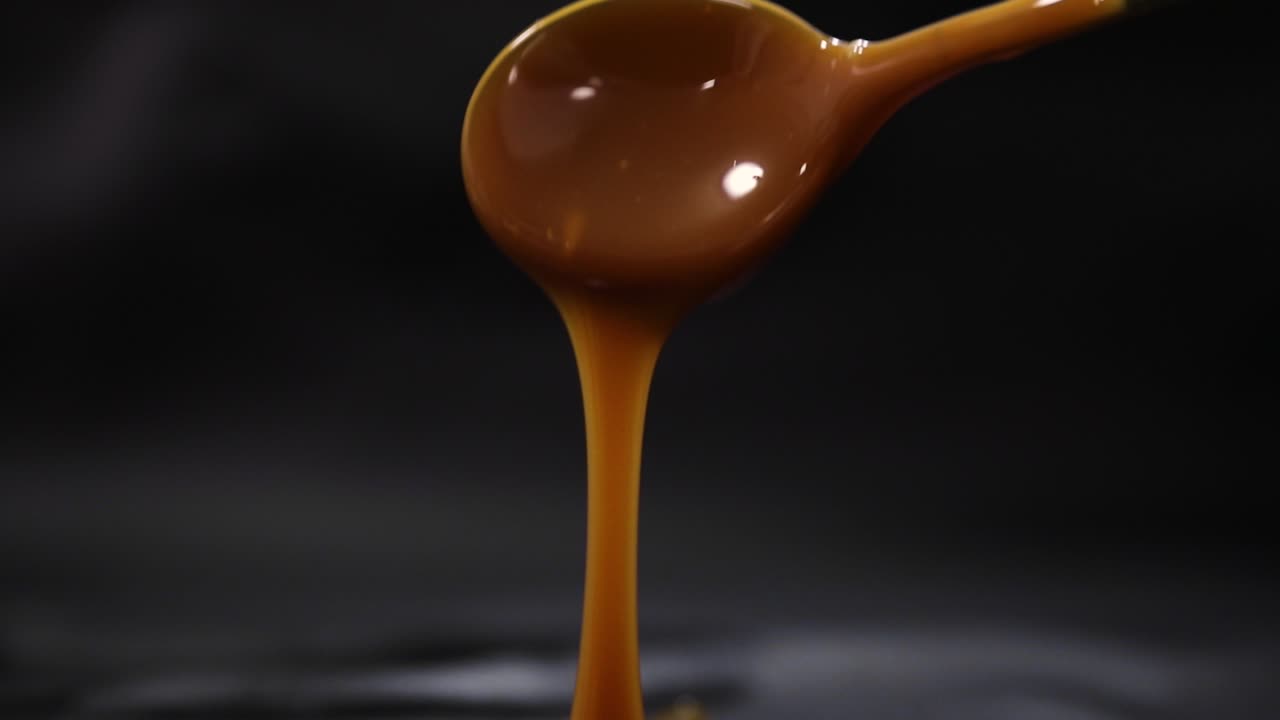 Tempting Creamy Caramel Spilling off Spoon with Black Background, Close up