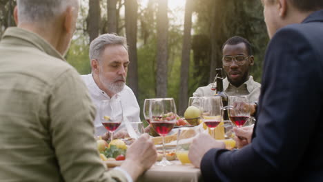 group of middle aged friends eating and talking to each other sitting at table during an outdoor party in the park 1