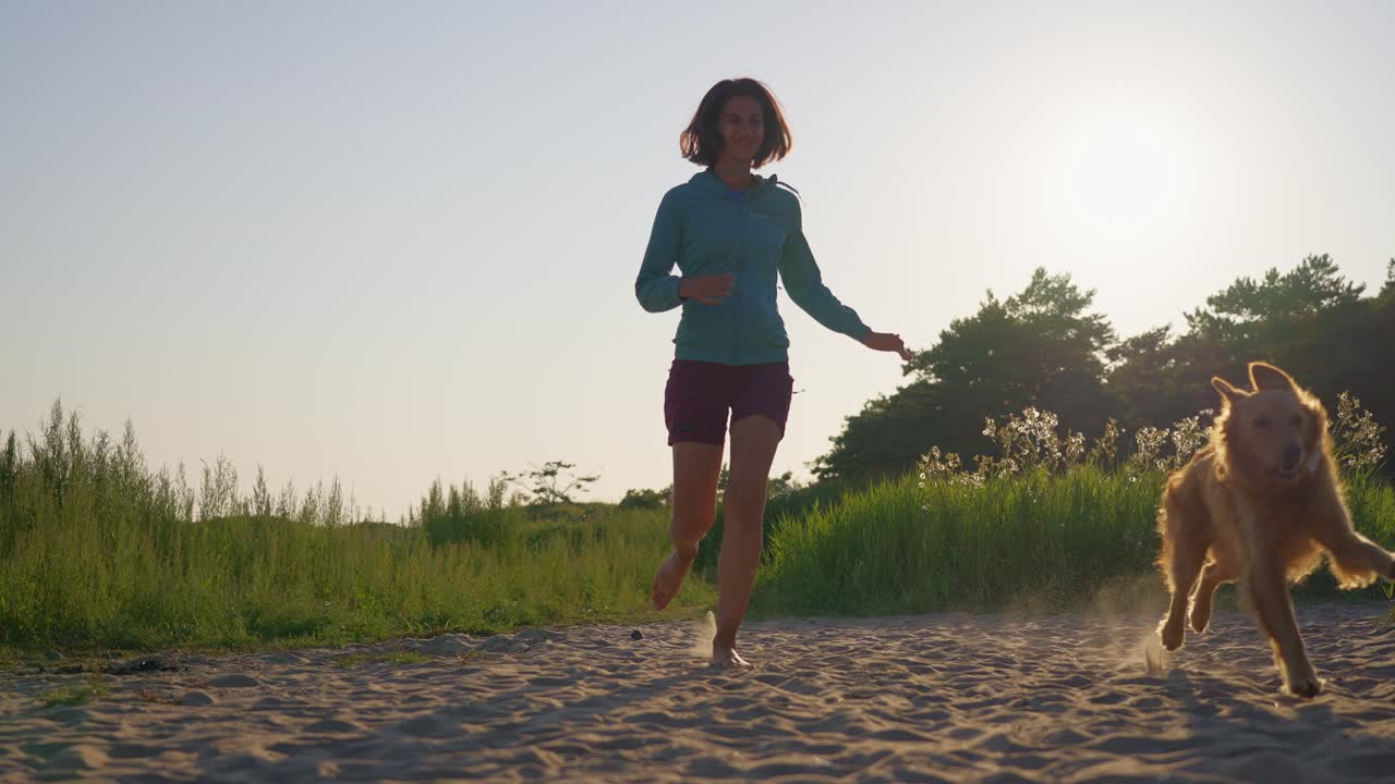 Woman running with a golden retriever along a sandy beach in the golden hour light