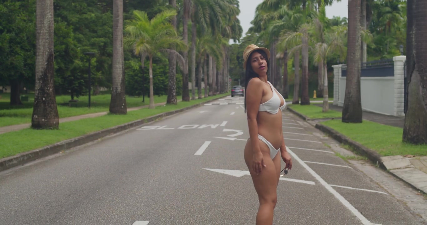Una ragazza in bikini bianco attira gli sguardi mentre passeggia per un colorato villaggio caraibico sul mare durante le riprese di un video.