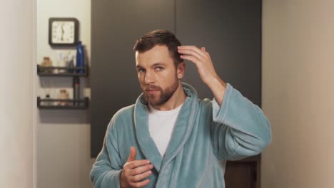 close-up portrait of a handsome man in a bathrobe examining his hair