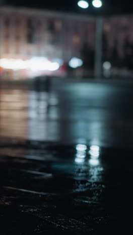 blurred view of cars passing on a wet city road at night, with vibrant reflections of lights on the pavement