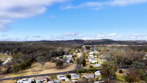 aerial footage captures a drone smoothly flying over a small australian town, revealing residential houses, tree-lined streets, and clear daytime skies with natural sunlight