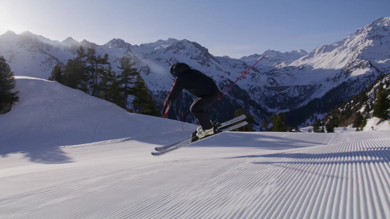 Sciatore che intaglia piste battute ad alta velocità a Nendaz, parte del comprensorio sciistico 4 Vallées nelle Alpi svizzere. Sci alpino d'élite con potenti spruzzi di neve e tecnica di precisione.
