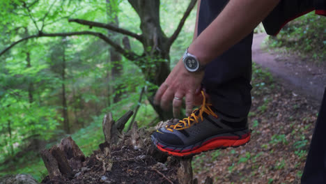 male hiker tying shoelace on green forest mountains at daytime. high angle