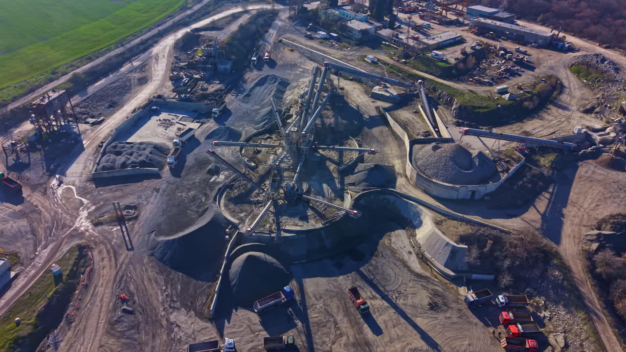 Heavy machinery operates in a large construction site with piles of materials under a clear blue sky
