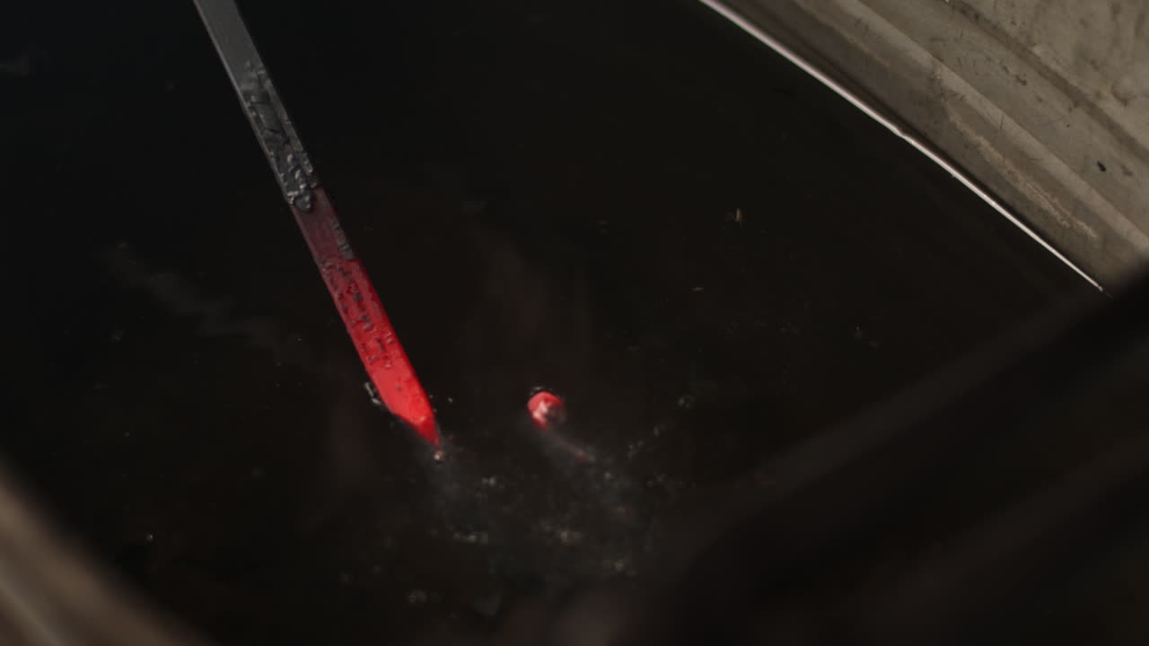 Blacksmith puts red hot metal into room temperature water as water bubbles in the workshop