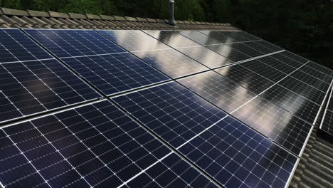 Aérea:-Conjunto-De-Colectores-De-Luz-Solar-En-El-Techo-De-Una-Casa,-Nubes-Reflejadas-Desde-La-Superficie