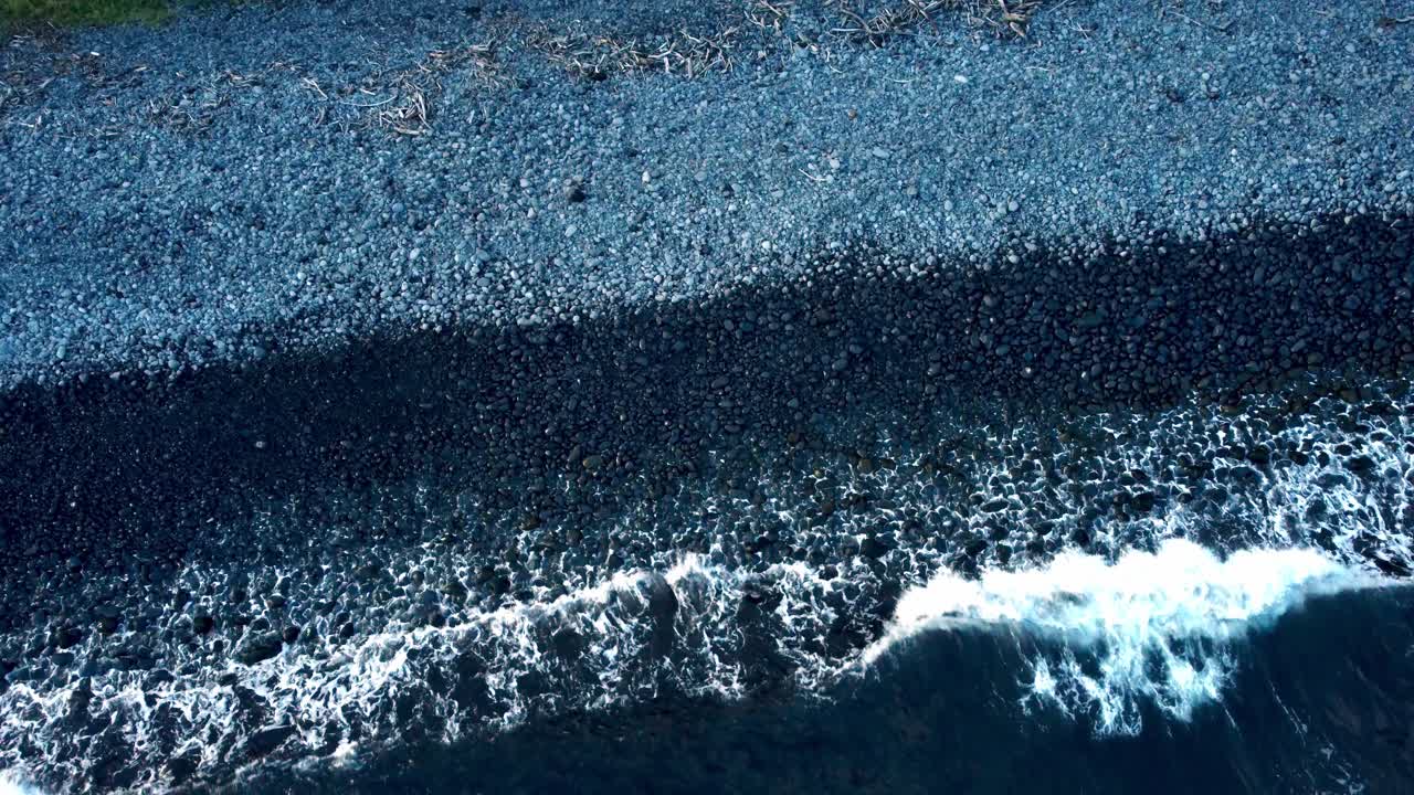 하와이 동부 마우이의 바위가 있는 해안은 드론의 관점에서 볼 때 화산암과 활기찬 푸른 바다 사이의 극적인 상호 작용을 드러내며, 울창한 열대 식물로 둘러싸여 있습니다.