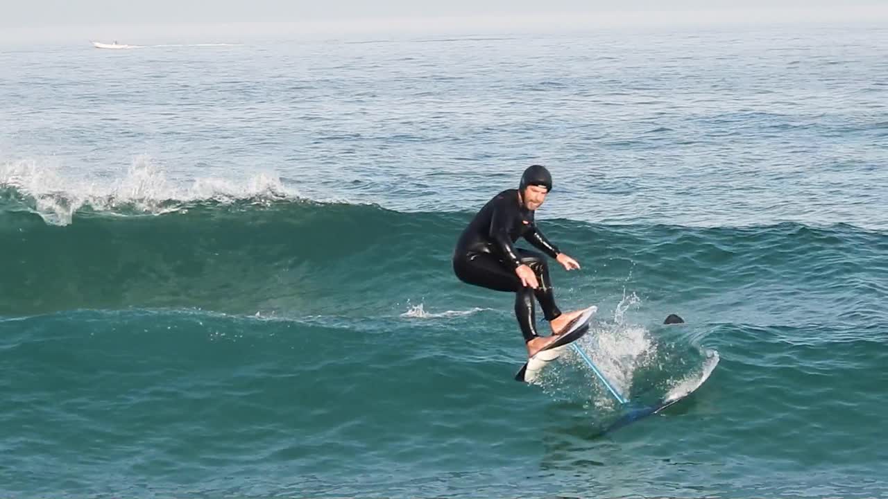 파란색 바다 파도를 타고 있는 하이드로포일 서프보드에 있는 서퍼의 가까운 움직임