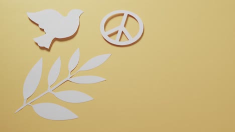 Close-up-of-white-dove-with-peace-sign-and-leaf-and-copy-space-on-yellow-background