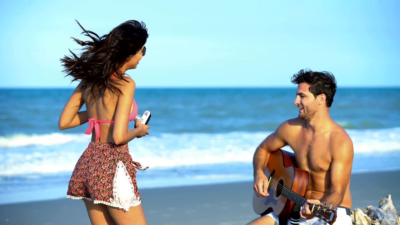 una mujer hispana tomando una selfie un hombre caucásico tocando la guitarra