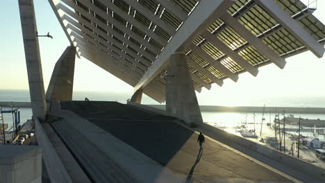 hombre irreconocible caminando bajo un enorme sistema fotovoltaico en el foro de barcelona