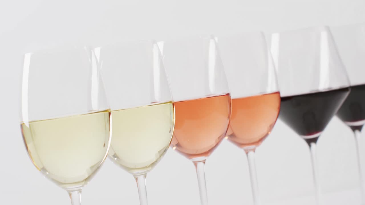 Fila de diversos tipos de vinos en copas sobre superficie blanca