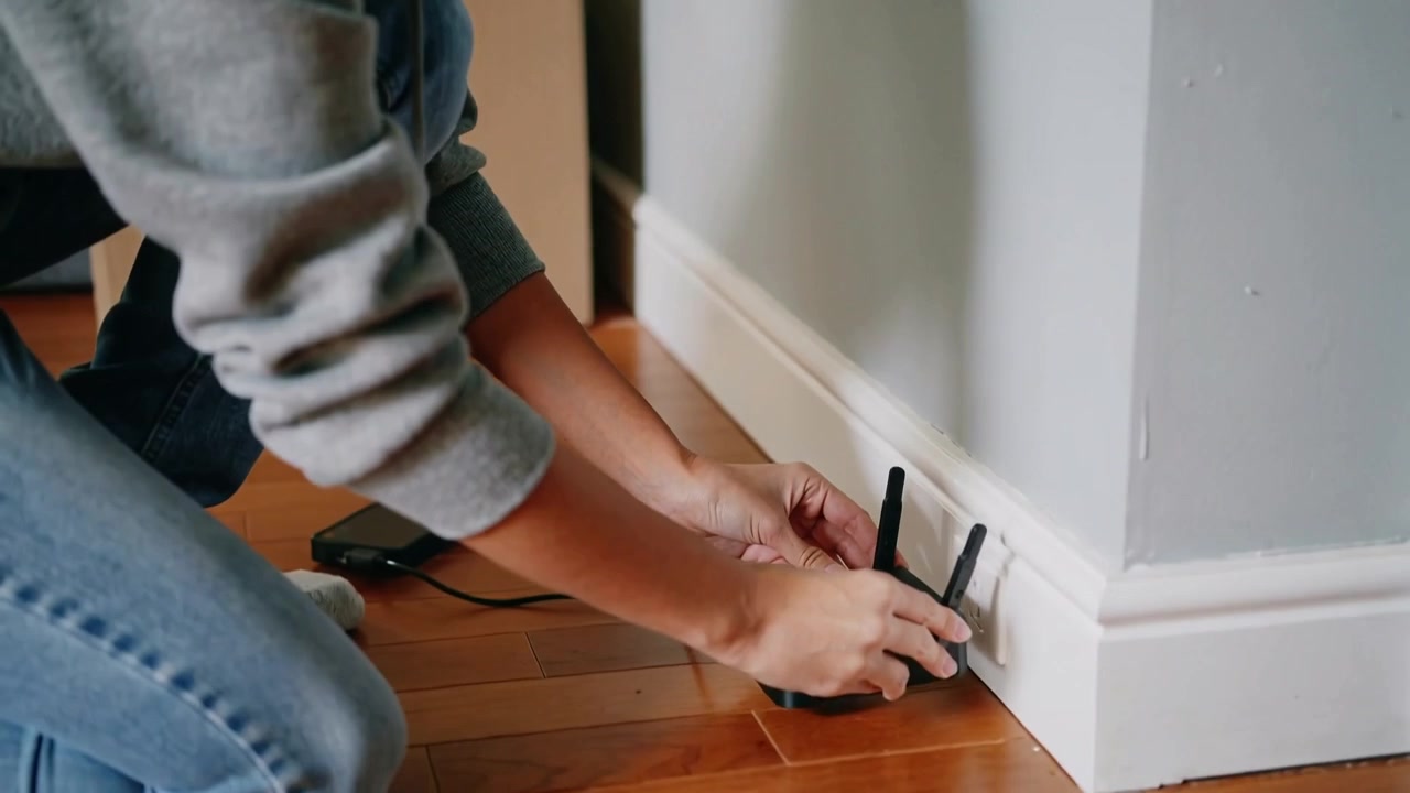 Unpacking box, kneeling woman in hoodie plugging router into outlet at home aligning antennas up