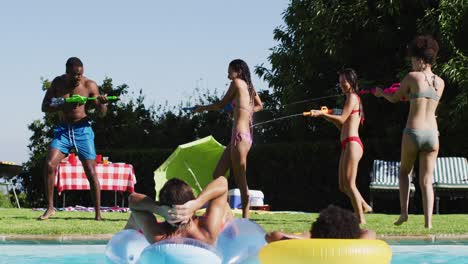 mixed race woman having fun playing with water guns in swimming pool