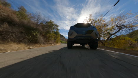 low fpv chasing shot of a new electric police car driving through the countryside