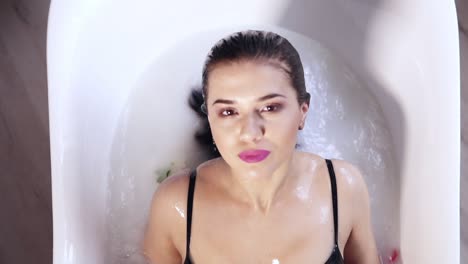 vista de cerca de una mujer joven bañándose en un baño de leche lleno de flores y levantándose tocando su cabello. concepto de spa y cuidado de la piel