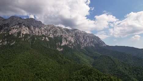 Piatra-craiului-mountains-with-lush-green-forest-under-blue-skies,-aerial-view