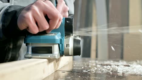 close-up of a carpenter's hand working with an electric plane in a home workshop