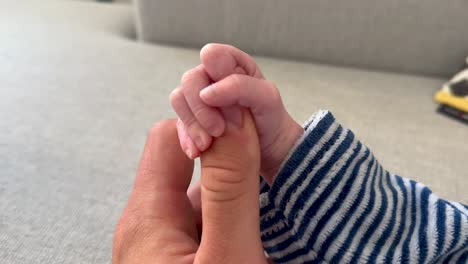 Strong-Baby-Hand-holding-finger-of-male-adult-on-couch-at-home-during-sunny-day