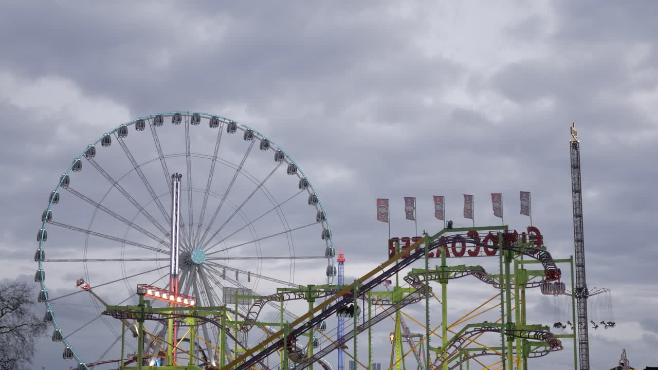 A large Ferris wheel and vibrant carnival rides in cloudy London, evoking excitement