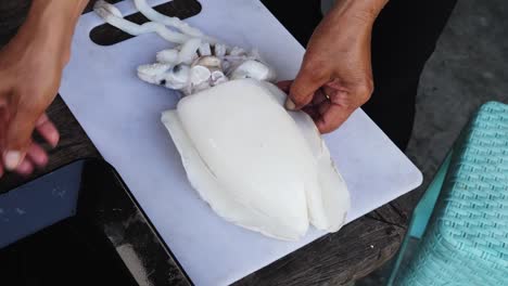 Chef-sets-fresh-squid-on-chopping-board-to-prepare-for-cutting,-close-up