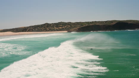 Aerial:-Surfing-the-beach-of-Bordeira-in-the-Algarve,-Portugal