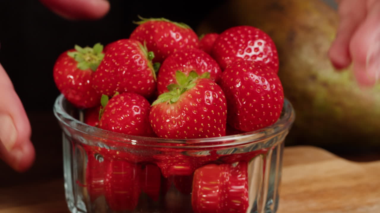 Hands Placing Fresh Strawberries in a Glass Bowl