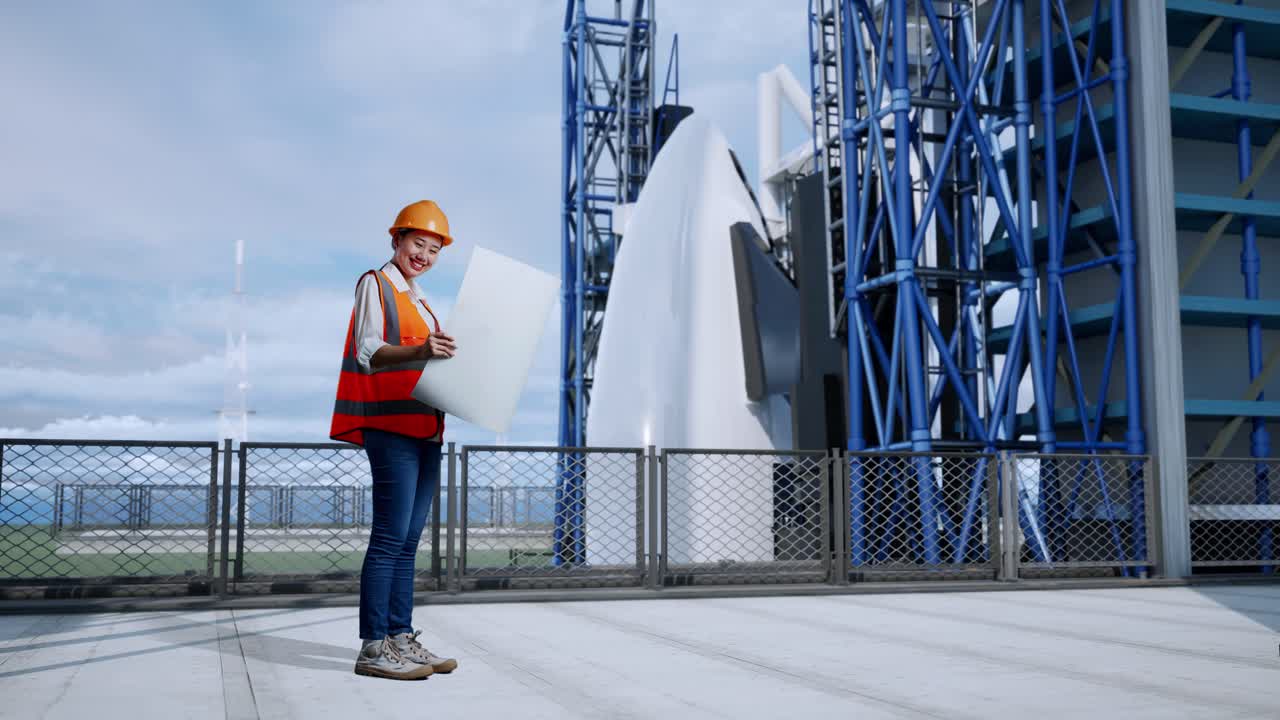 vista lateral completa del cuerpo de una ingeniera asiática con casco de seguridad mirando el plano en sus manos mientras está de pie con el transbordador espacial