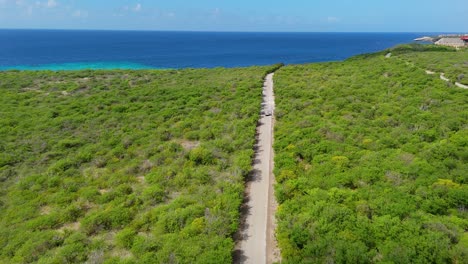 drone rises to reveal large suv bus van driving along sandy road to director's bay curacao