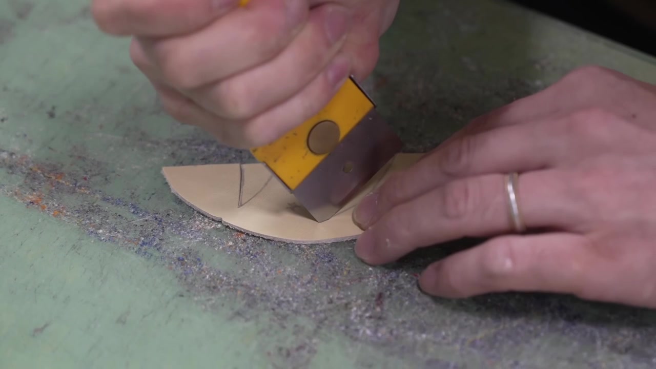 Worker marking a small leather glove component by hand with a pointed tool on the bench