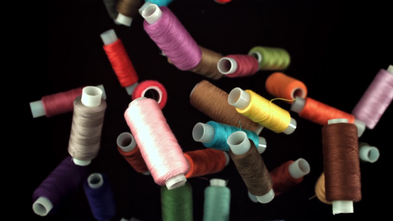 Colorful Spools of Thread Falling in Slow Motion on Black Background