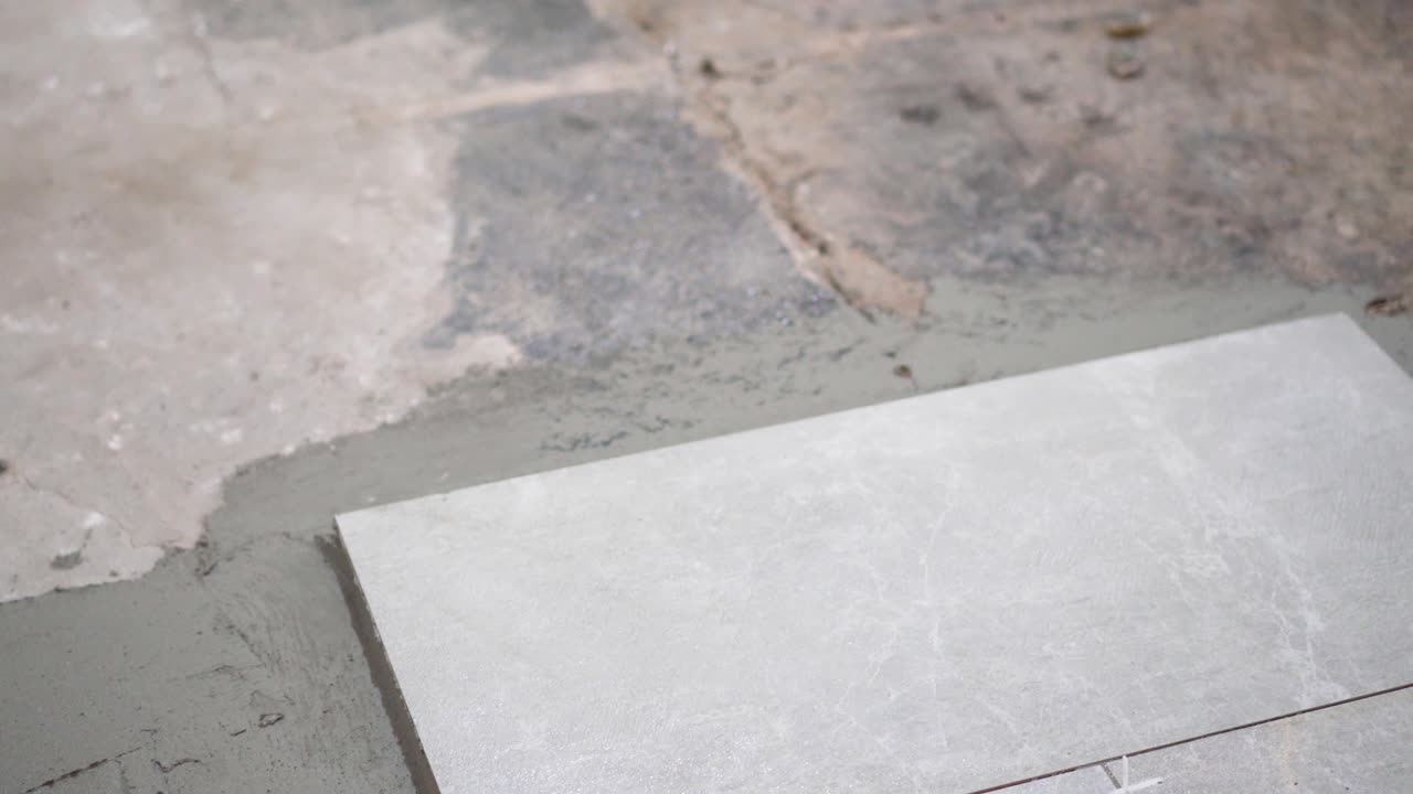 A close look at the construction tiler worker laying down the tile on cemented floor. Professional worker laying tiles on floor at construction site close-up slow motion.