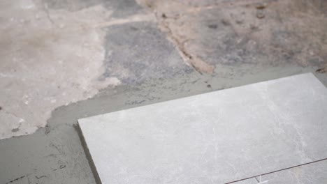 a close look at the construction tiler worker laying down the tile on cemented floor. professional worker laying tiles on floor at construction site close-up slow motion.