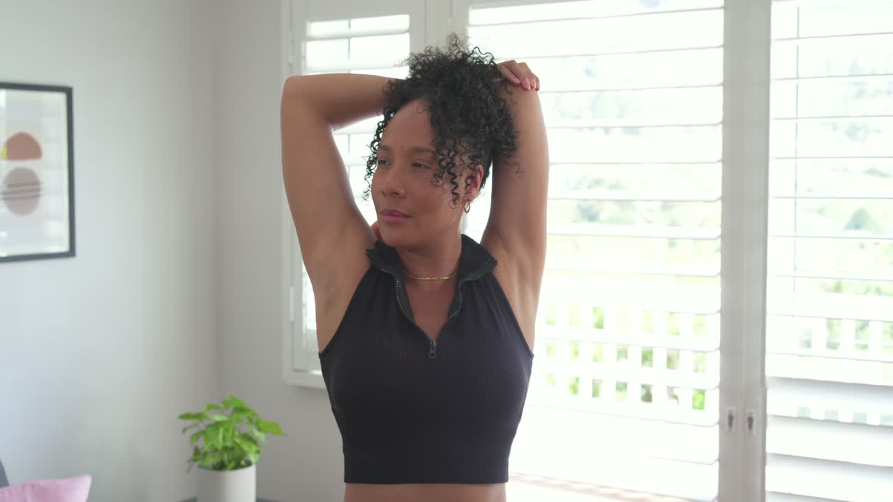 Afroamerikanische Frau in Sportkleidung macht Armübungen zum Aufwärmen in der Nähe von Fensterläden.