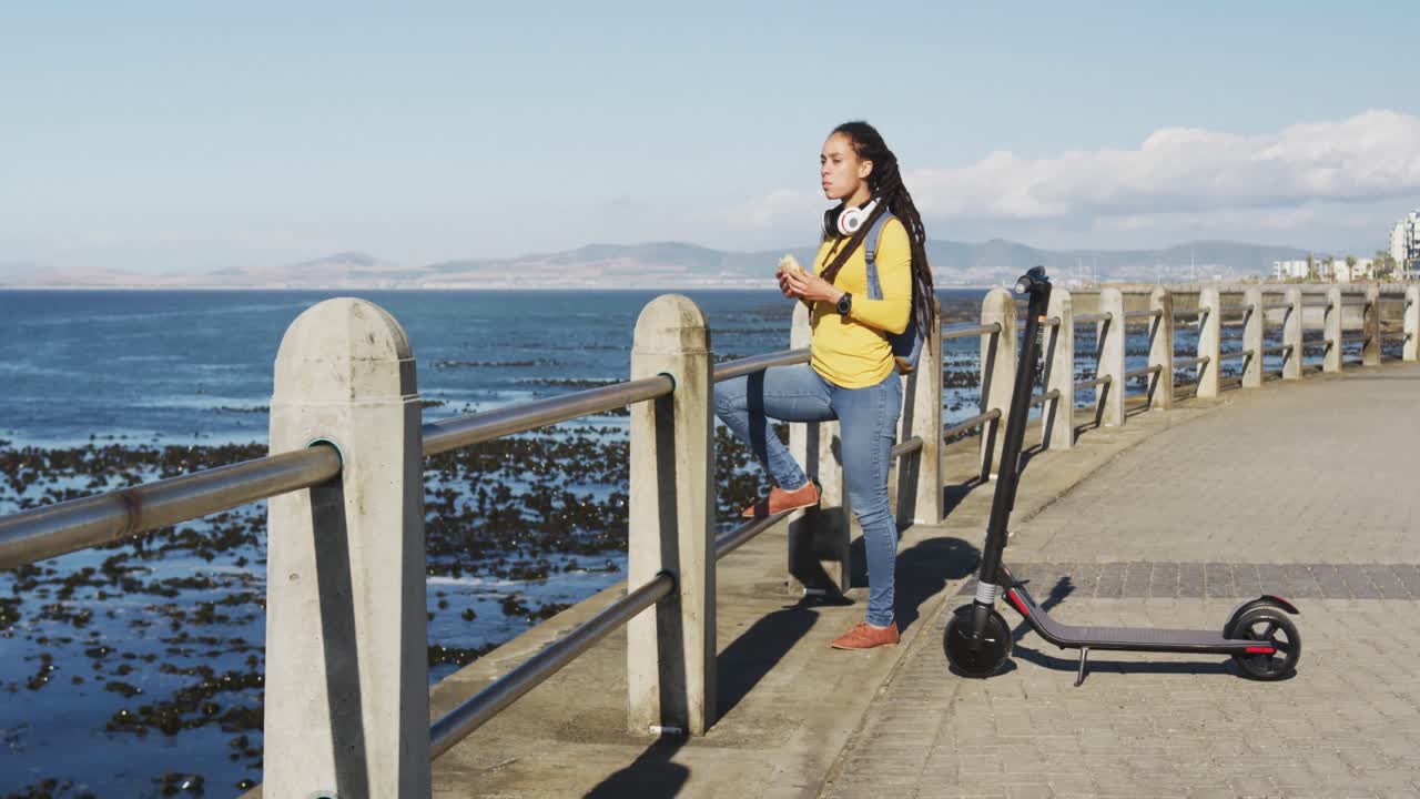 mujer afroamericana de pie comiendo sándwich paseo junto al mar