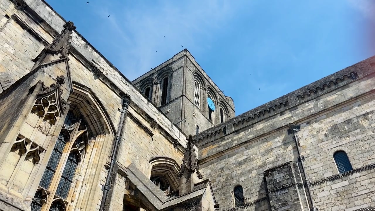 Cattedrale di Winchester con architettura gotica in pietra, torre della cattedrale, finestre ad arco, uccelli in volo e cielo blu a Winchester