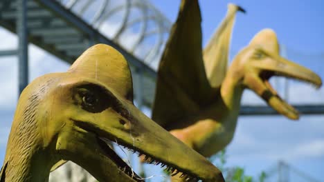 two pterodactyl ancient historic beasts realistic looking models with open mouths protecting their territory one of them moving his head from left to right mechanical creatures brown wooden sunny